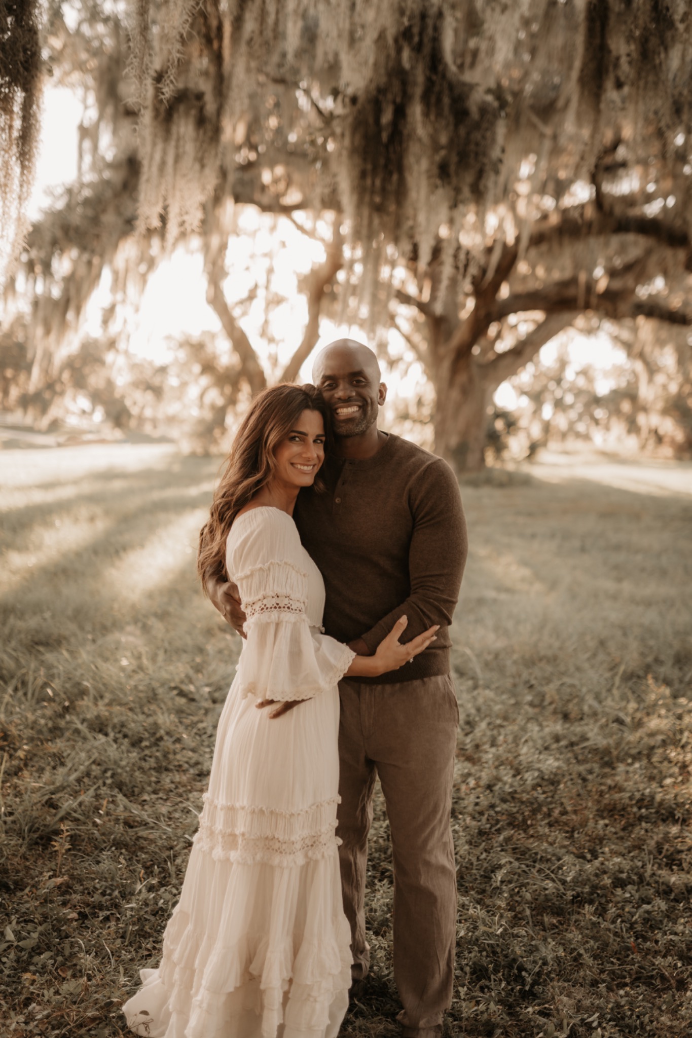 Sherman & Cristina Merricks embracing under a Spanish moss oak tree at golden hour